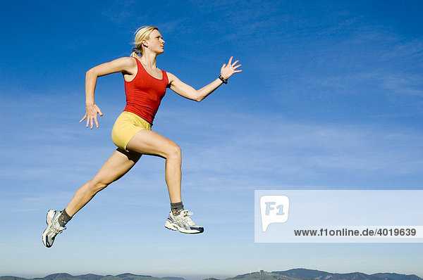 Blonde junge Frau springt beim Laufen in die Luft
