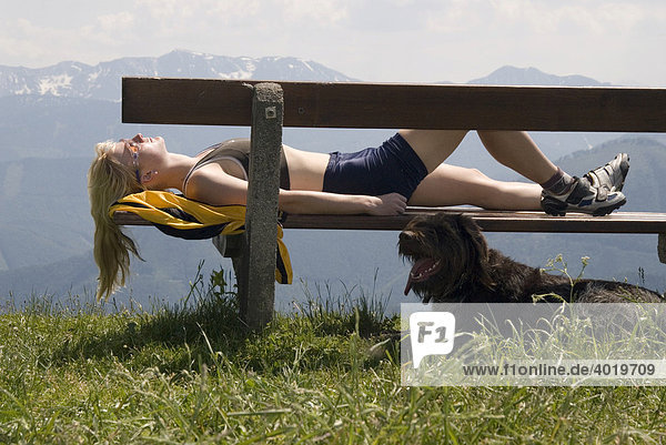 Eine Frau mit Hund macht eine Rast vom Wandern  liegt auf Bank