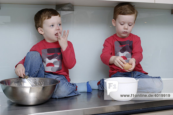 Zwillingsjungen  dreieinhalb Jahre alt  sitzen zum Backen auf der Küchenoberfläche