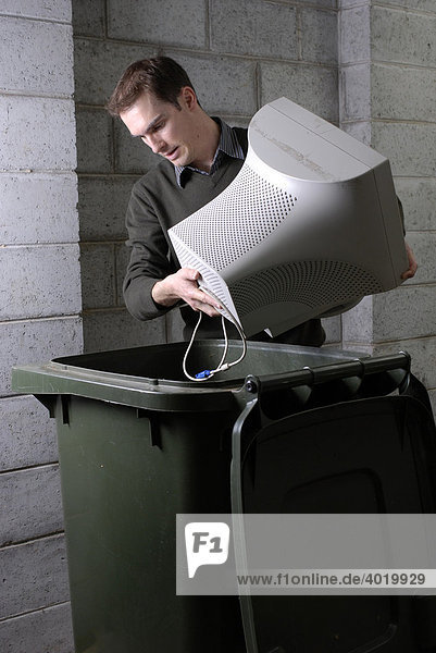 Man disposing of obsolete computer technology in a wheelie bin