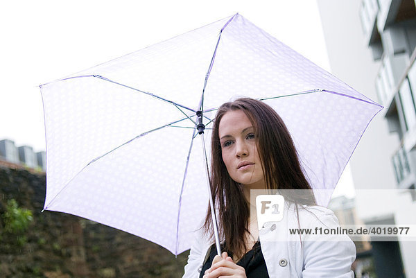 Junge Frau sucht Schutz unter einem Regenschirm an einem regnerischen Tag