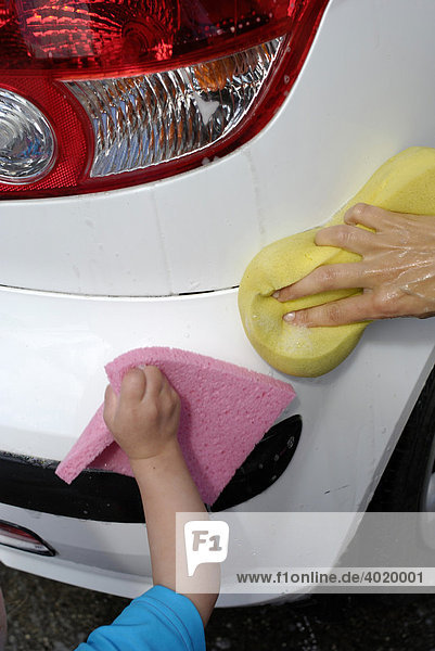 Zweijähriges Mädchen hilft ihrer Mutter beim Waschen des Familienautos