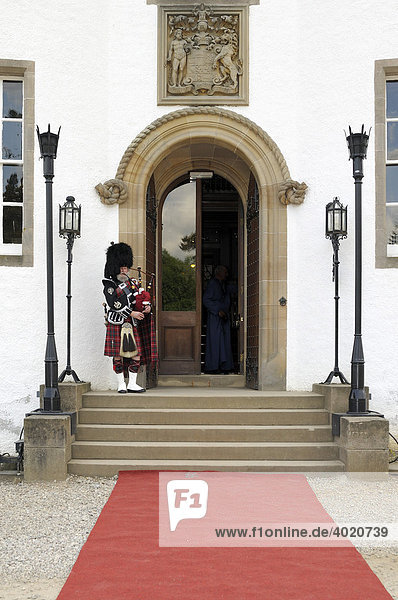 Bagpiper wearing a traditional Scottish costume with a bear skin hat and kilt at a castle entrance  Scotland  Great Britain  Europe