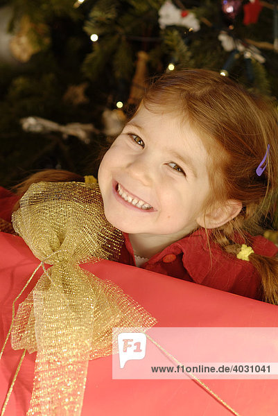 Kind mit einem großen Geschenk vor dem Weihnachtsbaum an Heiligabend