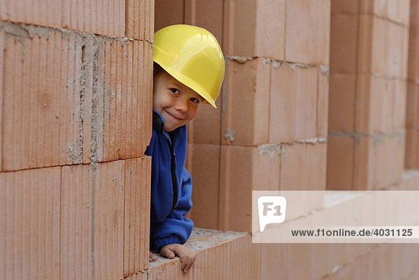 Kleiner Junge mit Bauhelm in einem Rohbau auf einer Baustelle