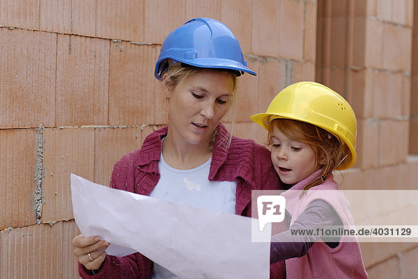 Mutter und Kind mit Bauhelmen studieren Bauplan in einem Rohbau auf einer Baustelle