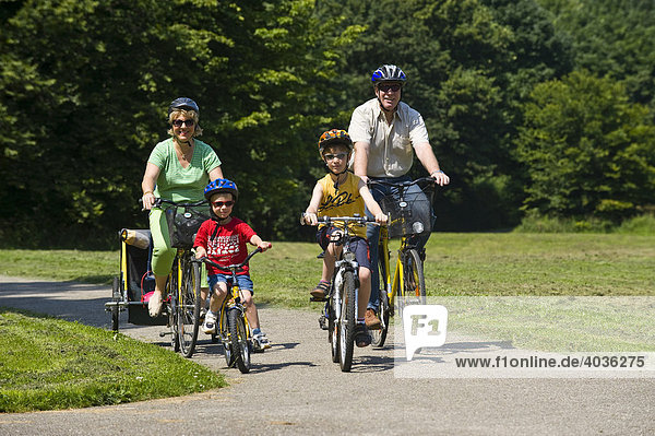 Familie mit 2 Kindern fährt mit Helmen auf Fahrrädern in Park