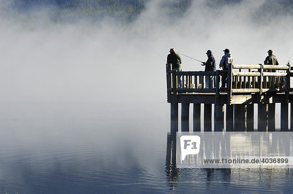 Fishermen casting from a dock into Trillium Lake on a foggy morning Trillium Lake  Oregon  USA
