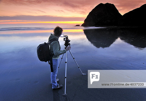 Kamerafrau mit Filmkamera filmt mit Stativ Sonnenuntergang am Meyers Creek Beach  Pistol River State Park  Oregon Küste  Oregon  USA  Nordamerika
