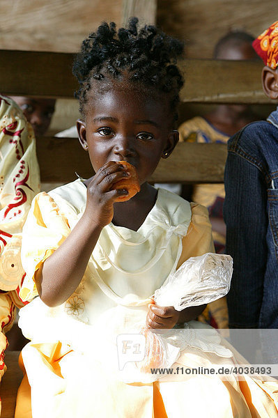 A girl eating a bread roll during church service  Manyemen  Cameroon  Africa