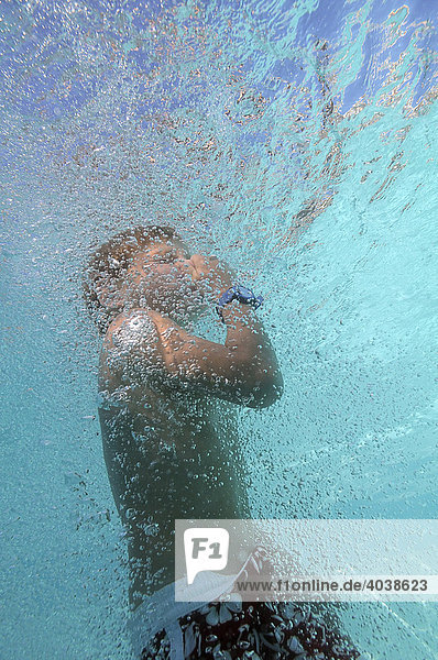 6-jähriger Junge ist im Wasser von Luftblasen umgeben und hält sich die Nase zu  Unterwasseraufnahme  Villasimius  Sardinien  Italien  Europa