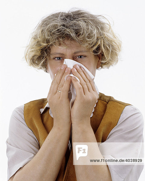 A blond woman is blowing her nose with a paper tissue  cold  allergy