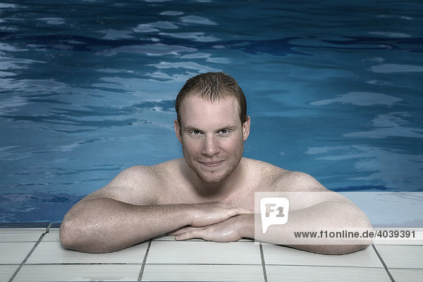 Junger Mann lehnt am Beckenrand im Schwimmbad