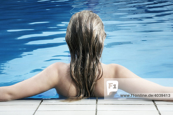 Junge dunkelblonde Frau lehnt am Beckenrand im Schwimmbad