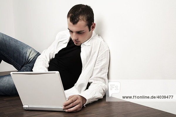 Young man sitting on the floor  working on his laptop