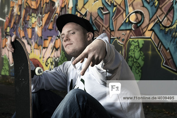 Junger Mann mit Skateboard vor einer Graffitiwand