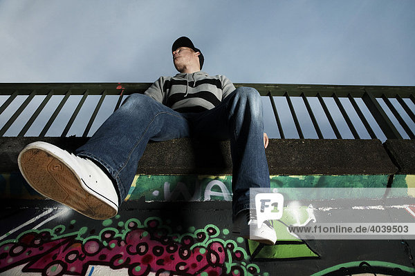 Junger Mann sitzt auf einer mit Graffiti besprühten Wand