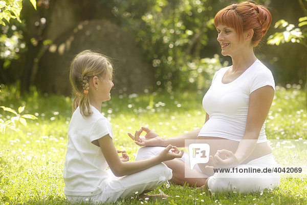 Mädchen und schwangere Frau in Yoga-Position im Garten