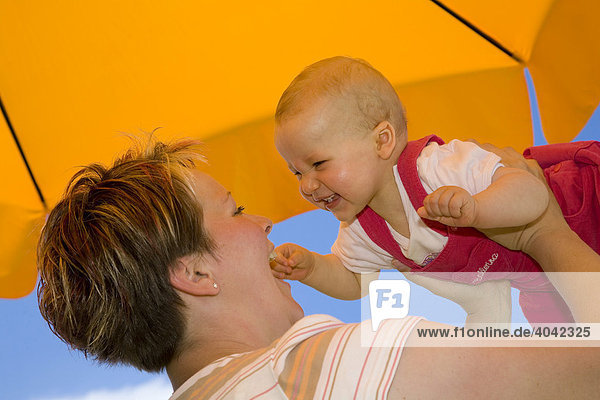 Mutter mit Baby  10 Monate  spielen unter Sonnenschirm