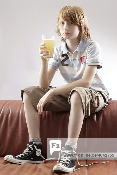 12-jähriger Junge sitzt auf Sofa  mit Saftglas