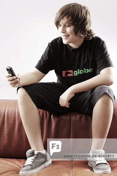 14-jähriger Junge mit Handy  auf Sofa  lacht