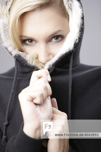 Junge blonde Frau in schwarzer Jacke mit Kapuze