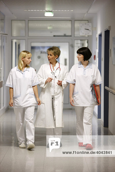 Female doctor talking to two nurses in a hospital ward corridor