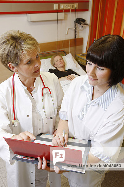 Ärztin und Krankenschwester besprechen sich bei einer Visite im Krankenzimmer einer Patientin in einem Krankenhaus