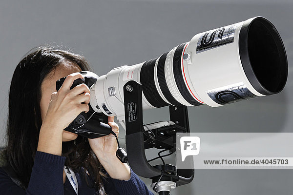 Junge Frau schaut durch Digitalkamera mit Superteleobjektiv  Canon Messestand  Photokina  Köln  Nordrhein-Westfalen  Deutschland  Europa