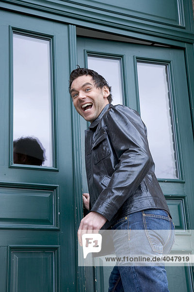 Lachender junger Mann in Lederjacke an einer grünen Haustüre