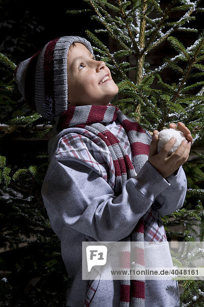 A boy with a snow ball in his hands looking upqq