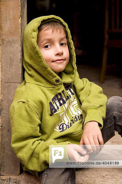 Kleiner Junge in grünem Kapuzenshirt sitzt am Eingang einer Wanderhütte