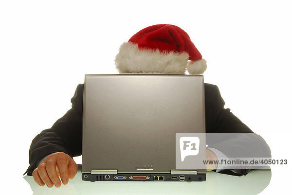 Businessmann hinter Laptop mit Weihnachtsmannmütze