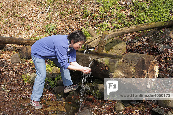 Frau erfrischt sich an Brunnen  Eisgraben  Naturschutzgebiet Lange Rhön  Unterfranken  Bayern  Deutschland  Europa