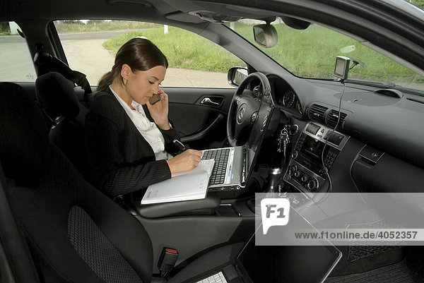 Young businesswoman in her car with laptop  agenda and mobile phone