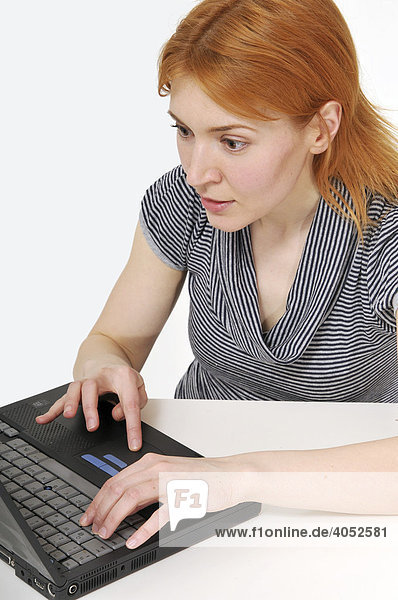 Attractive  red-headed woman sitting at a table with a laptop  concentrating on her work  surfing the web