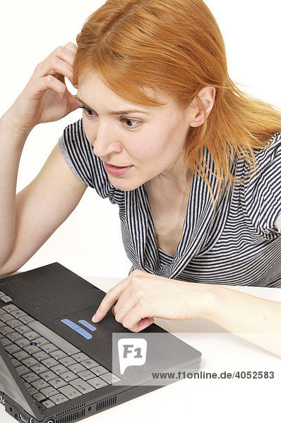 Rothaarige  attraktive Frau mit Laptop am Tisch  arbeitet konzentriert  surft  Internet  erstaunt  gespannt