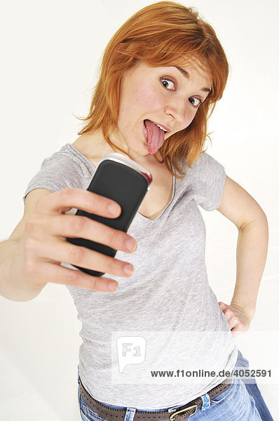 Rothaarige  attraktive Frau macht Foto mit Handy  streckt Zunge heraus  frech