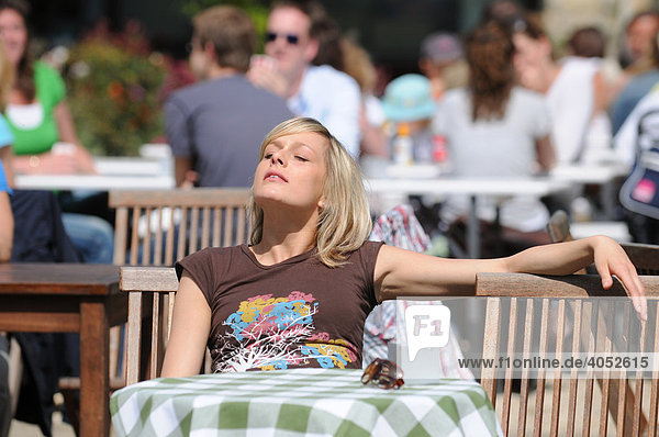 Junge blonde Frau sitzt in Café  sonnt sich  entspannt  Sommer