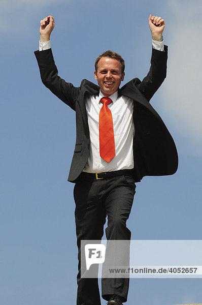 Geschäftsmann im Anzug mit roter Krawatte streckt Arme in die Luft und jubelt  Erfolg  Sieg  Freude