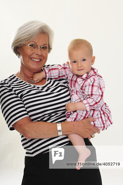 Portrait sportliche Frau  60  Seniorin mit grauen Haaren  Brille  in Freizeitkleidung  mit Enkel  Enkeltochter  Baby auf dem Arm  lachen