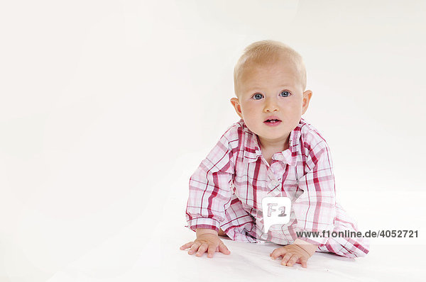 Baby  9 Monate  mit rosa kariertem Kleid krabbelt auf dem Boden auf Kamera zu