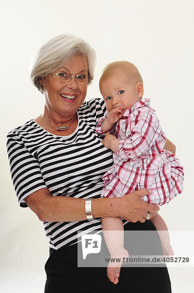 Portrait symphathische Frau  60  Seniorin  mit grauen Haaren hat Enkeltochter  Baby auf dem Arm