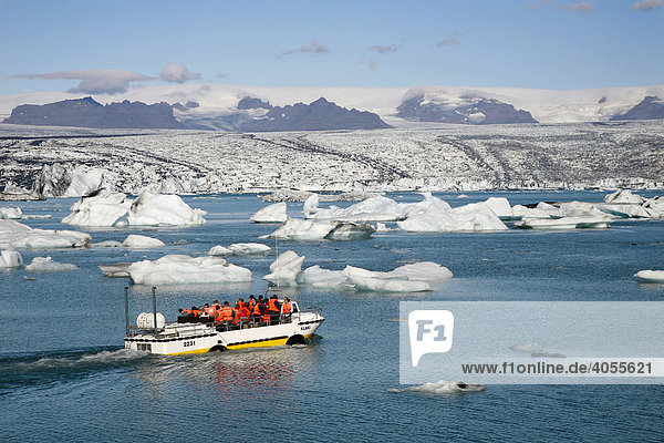 In the Joekulsarlon glacier lagoon of the Vatnajoekull Glacier  people travelling in an boat between the floating icebergs  which are partly coloured by black lava ash  at back the Vatnajoekull glacier tongue  Iceland  Europe
