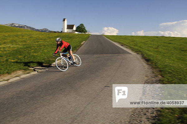 Racing cyclists riding on a country road past a church  Steinkirchen  Chiemgau  Bavaria  Germany  Europe