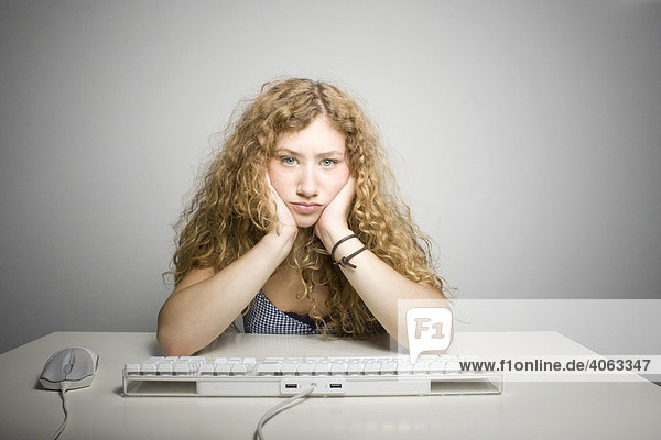 Junge langhaarige Frau sitzt frustriert vor einer Computertastatur am Tisch
