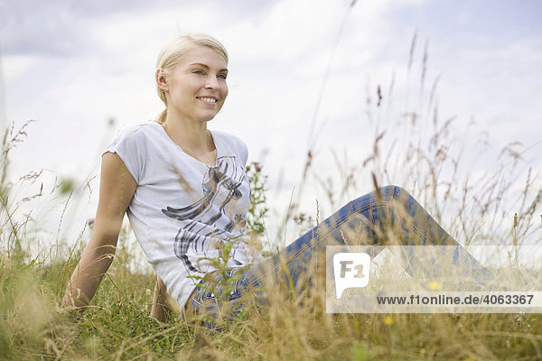 Young blonde woman sitting in long grass