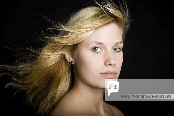 Junge blonde Frau mit langen wehenden Haaren vor Schwarz