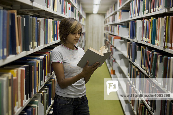 Junge dunkelhaarige Frau  Studentin  blättert in einem Buch zwischen den Bücherregalen in der Bibliothek