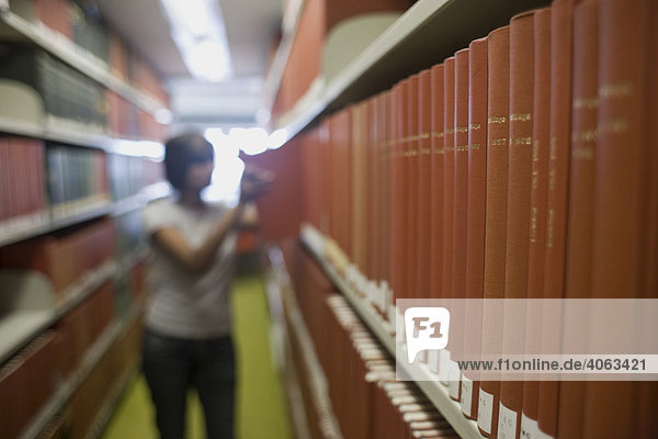 Bücherregal in einer Bibliothek  hinten greift eine junge Frau nach einem Buch